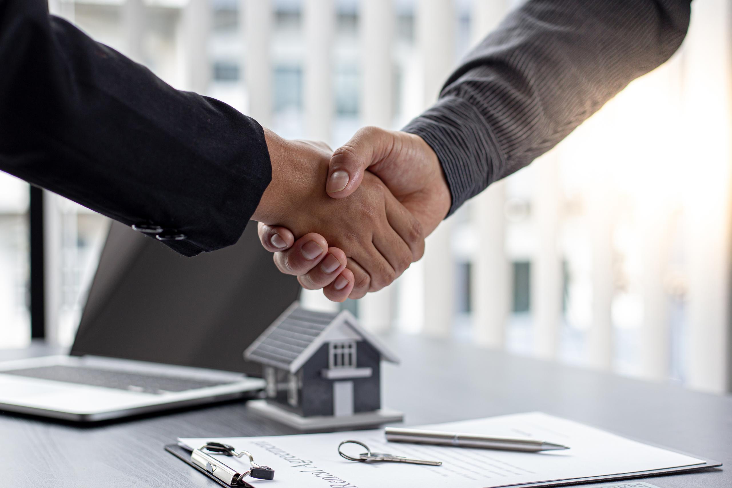 Professioneller Händedruck im Büro über einem Immobilienvertrag und Hausmodell nach der erfolgreichen Ermittlung des Werts über das Ertragswertverfahren für eine Gewerbeimmobilie.