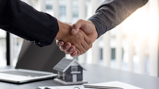 Professioneller Händedruck im Büro über einem Immobilienvertrag und Hausmodell nach der erfolgreichen Ermittlung des Werts über das Ertragswertverfahren für eine Gewerbeimmobilie.