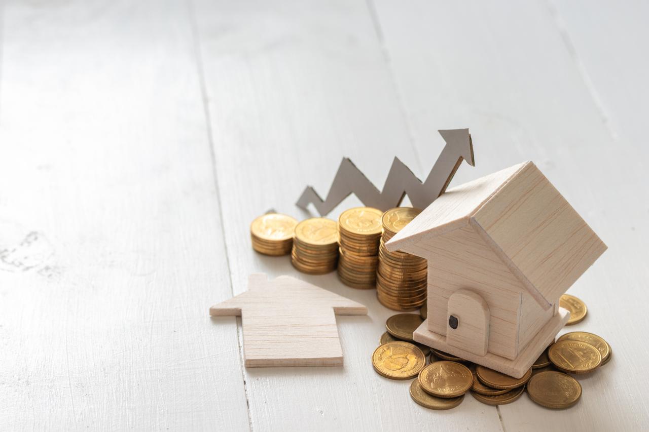 Ein kleines Holzhaus auf einem Haufen Goldmünzen neben einer ansteigenden Münzkurve mit Pfeil – Symbolisiert den steuerlichen Gewinn aus dem Verkauf einer Gewerbeimmobilie und die Einhaltung der Spekulationsfrist.